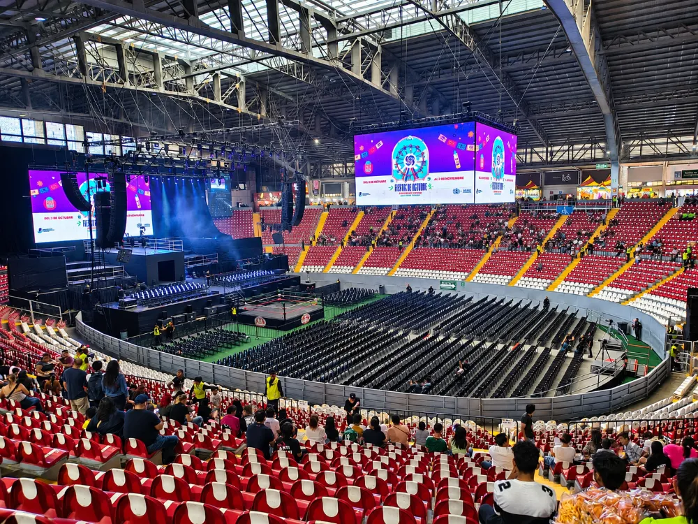 Escenario de las Fiestas de Octubre en Guadalajara con ring de lucha libre y pantallas LED en arena con gradas rojas