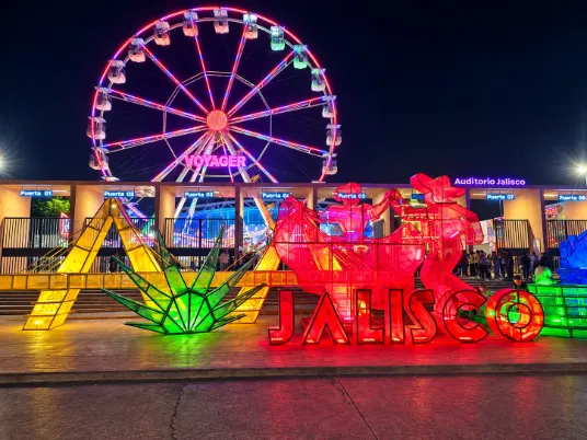 Entrada de las Fiestas de Octubre en Guadalajara con letrero luminoso de Jalisco y rueda de la fortuna Voyager de noche